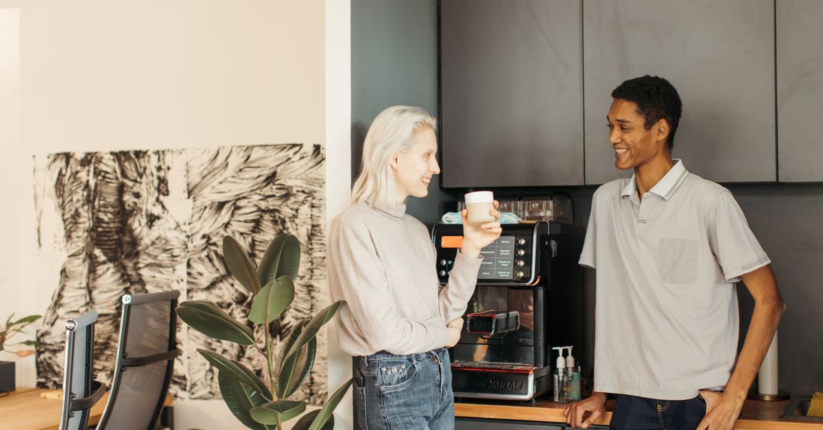 Coworkers enjoying a light conversation over coffee in a modern office kitchen.