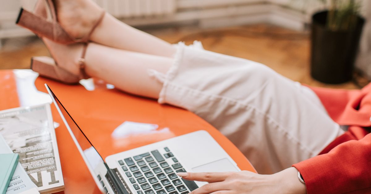 Woman wearing heels and working on a laptop at home, relaxed and casual setting.